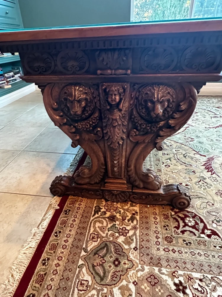 Detail view of a substantial statement table with an elaborately carved pedestal base and carved apron.